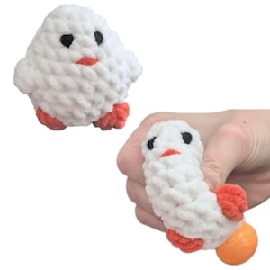 May include: White plush chick toy with orange feet and black eyes. The chick is being squeezed in a hand, revealing an orange ball inside.