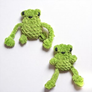 Könnte beinhalten: Zwei grüne Plüschfrosch-Spielzeuge mit schwarzen Augen und Mäulern werden vor einem weißen Hintergrund gezeigt. Die Frösche haben ausgestreckte Arme und Beine und ein strukturiertes, flauschiges Aussehen. Die Spielzeuge sind handgefertigt.
