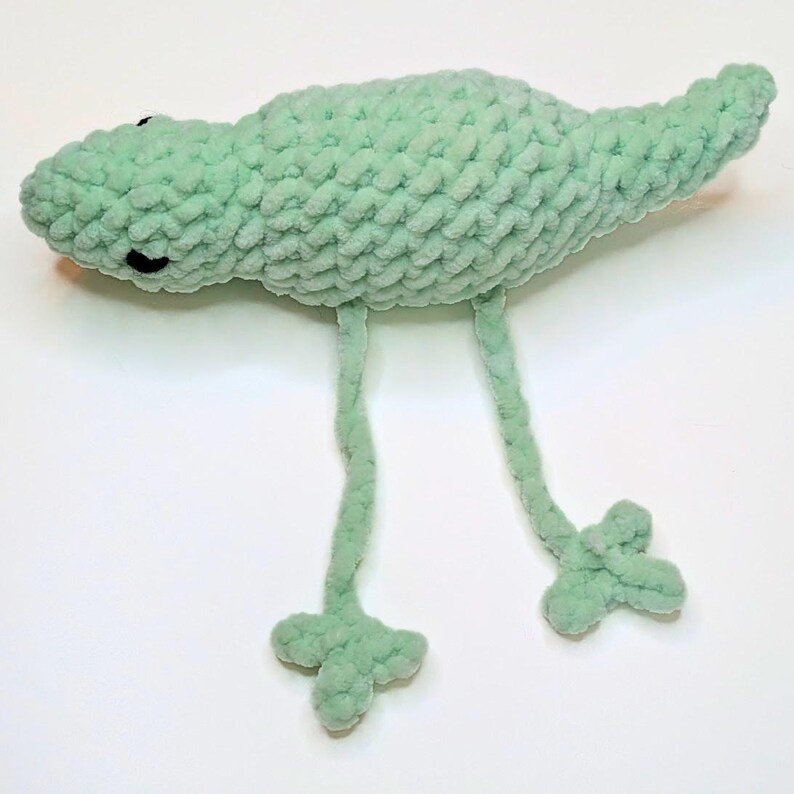 Side view of a mint green crochet lizard with long legs. The legs can be pulled back and forth to create a fidget toy.