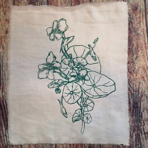 Könnte beinhalten: Ein quadratischer, cremefarbener Stoff mit einem grünen Blumendesign. Das Design zeigt detaillierte Strichzeichnungen von Blumen, Blättern und Ranken. Der Stoff hat einen rohen, unfertigen Rand, vor einem Holzgrund.