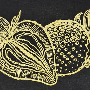 Könnte beinhalten: Goldfarbene Illustration von zwei Erdbeeren auf schwarzem Hintergrund. Eine Erdbeere ist halbiert und zeigt das Innere. Die andere ist ganz. Beide haben detaillierte Blatt- und Samenmuster. Botanischer Stil.