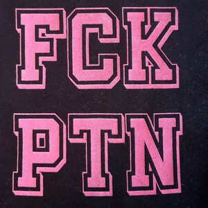 Könnte beinhalten: Rosa Buchstaben, die "FCK PTN" auf schwarzem Hintergrund buchstabieren.