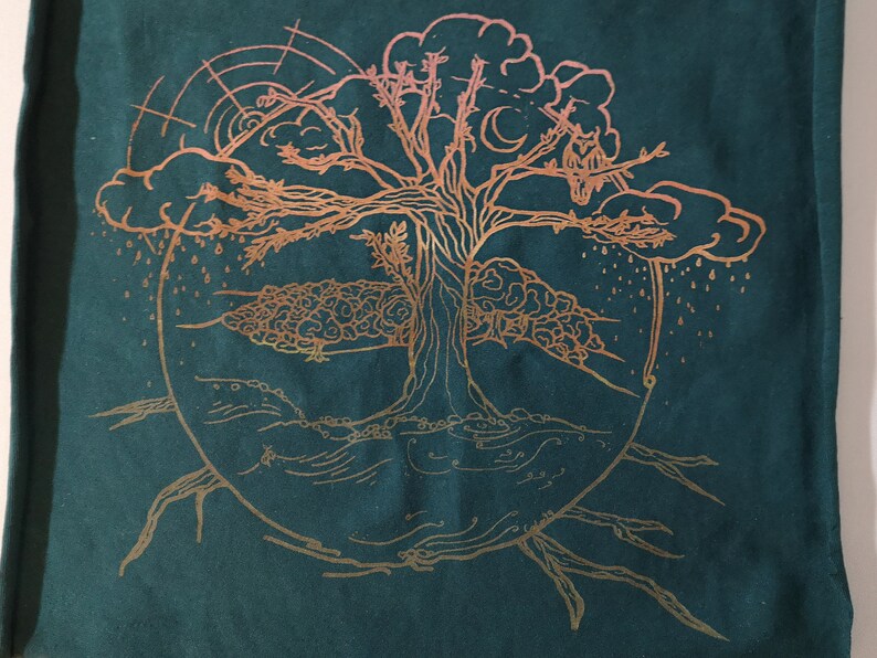 Pu&ograve; includere: Un disegno dorato ad albero della vita su uno sfondo di tessuto verde scuro. L'albero ha un tronco spesso e rami con foglie. Il disegno include una nuvola, la pioggia e una luna crescente.