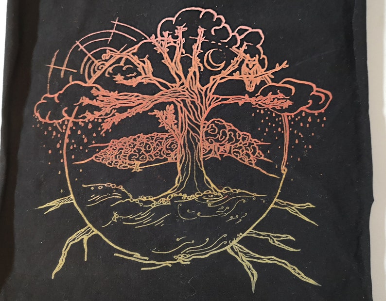 Pu&ograve; includere: Una borsa di tela nera con un'illustrazione colorata e dettagliata di un albero con una nuvola e pioggia. L'albero &egrave; delineato in oro e ha un gradiente di rosso, arancione e giallo.