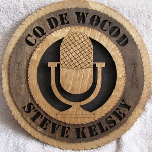 May include: A wooden plaque with a microphone design and the text "CQ DE WOCOD STEVE KELSEY". The plaque has a brown wood background with a black circle in the center.
