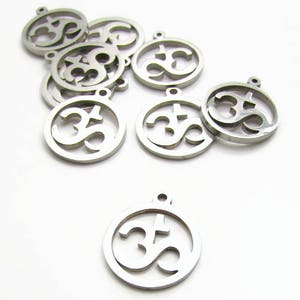 May include: A set of silver metal charms featuring the Om symbol. The charms are round and have a hole at the top for attaching to a necklace or bracelet.