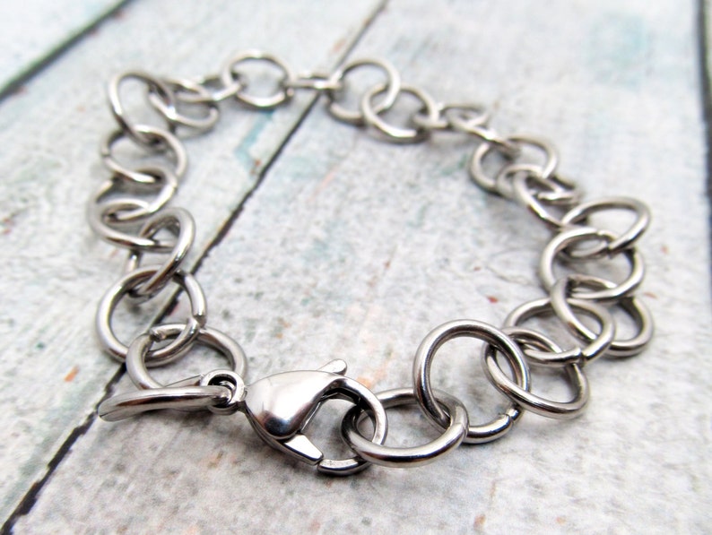 May include: A silver chain bracelet with a lobster clasp fastening. The bracelet is made of interlocking metal rings.
