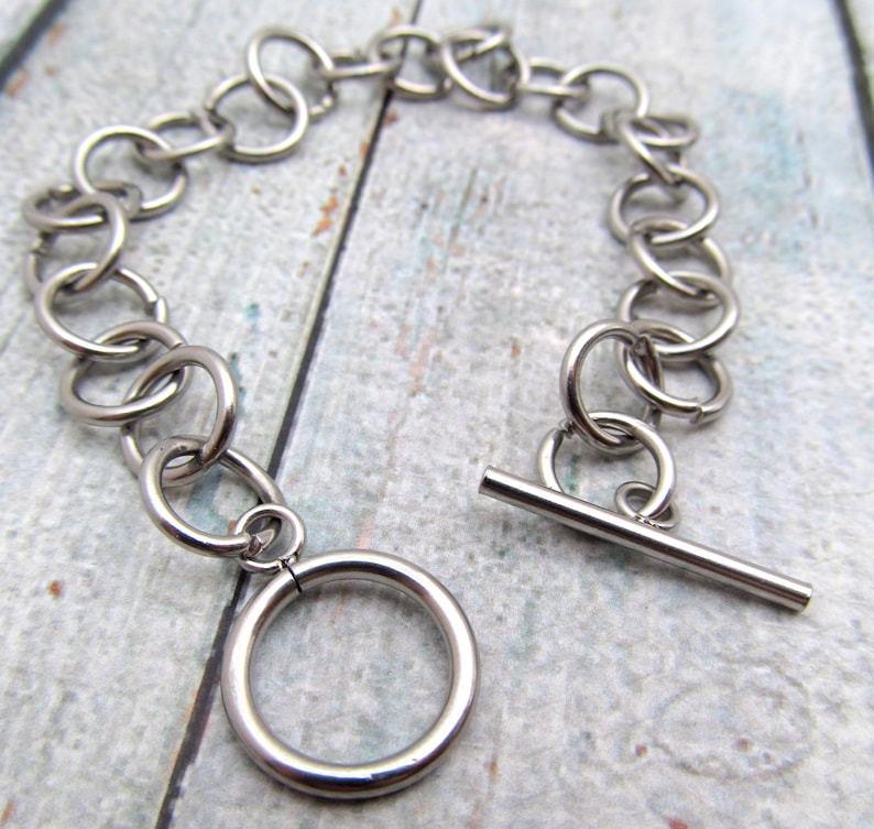 May include: A silver chain bracelet with a t-bar clasp. The chain is made of interlocking circles.