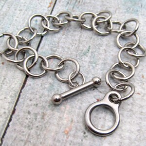 May include: A silver chain bracelet with a toggle clasp. The chain is made of interlocking metal rings.