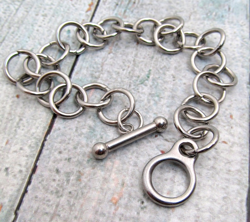 May include: A silver chain bracelet with a toggle clasp. The chain is made of interlocking metal rings.