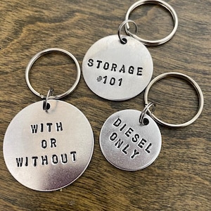 May include: Three silver keychains with round metal tags. The tags have the text "STORAGE #101", "WITH OR WITHOUT", and "DIESEL ONLY" engraved on them.