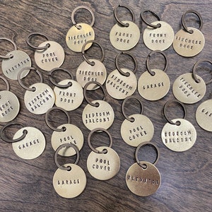 May include: A collection of brass keychains with different labels, including "Front Door", "Bedroom Balcony", "Pool Cover", "Garage", "Elevator", and "Tischler Door".