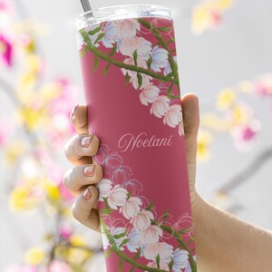 May include: A maroon tumbler with a floral design and the name "Noelani" in cursive. The tumbler features a pattern of white and light blue flowers with green stems. A silver straw is visible at the top.