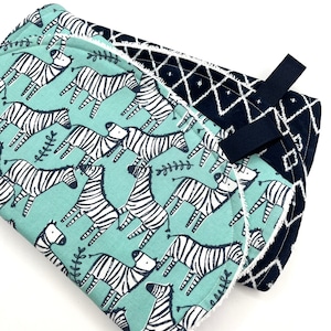 May include: A baby burp cloth with a blue and white zebra print on one side and a black and white geometric pattern on the other side. The cloth has a black strap for easy carrying.
