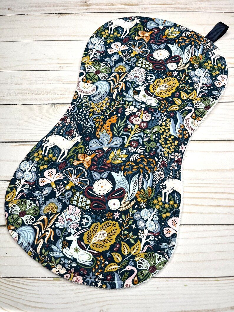 May include: A dark blue pot holder with a white, yellow, and green floral pattern featuring deer, birds, and other woodland creatures.