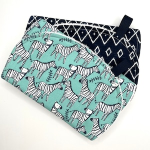 May include: Two kitchen towels, one with a black and white geometric pattern and the other with a green background and a black and white zebra print.