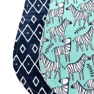 May include: Two reversible baby bibs. One side is a blue and white geometric pattern. The other side is a light blue background with a white zebra print.