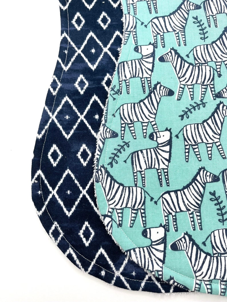 May include: Two reversible baby bibs. One side is a blue and white geometric pattern. The other side is a light blue background with a white zebra print.