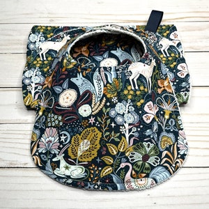 May include: A dark blue fabric bib with a white scalloped edge. The bib features a whimsical woodland pattern with deer, foxes, and birds in shades of white, brown, and green.