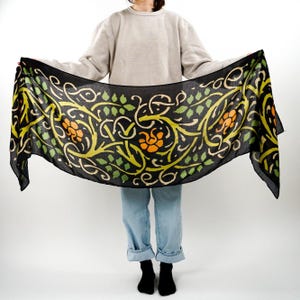 May include: A black scarf with a green and orange floral pattern. The pattern features stylized leaves and flowers.