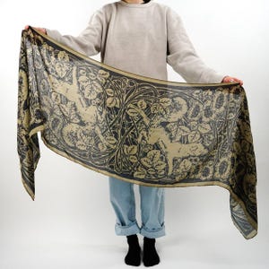 May include: A black and gold silk scarf with a repeating pattern of stylized rabbits and leaves. The scarf is being held by a person.