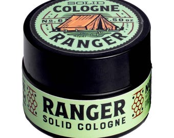 Op de afbeelding: Een kleine zwarte ronde houder met Ranger vaste cologne. Het deksel heeft een lichtgroen etiket met een tentillustratie, de tekst SOLID COLOGNE, RANGER, No. 6 en 14g. Het zij-etiket herhaalt de productnaam in zwarte letters.