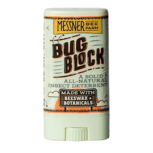 May include: A light green solid insect repellent stick with the text "BUG BLOCK" in large, bold letters. The label also includes "MESSNER BEE FARM" and states it's made with beeswax and botanicals.