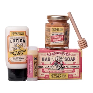 May include: A Messner Bee Farm gift set including a 2 oz bottle of Honeysuckle Vanilla hand and body lotion, a Hibiscus Lime lip balm, a jar of Strawberry Rhubarb creamed honey with a wooden dipper, and a 4 oz Pink Clay Salt and Honey bar soap.
