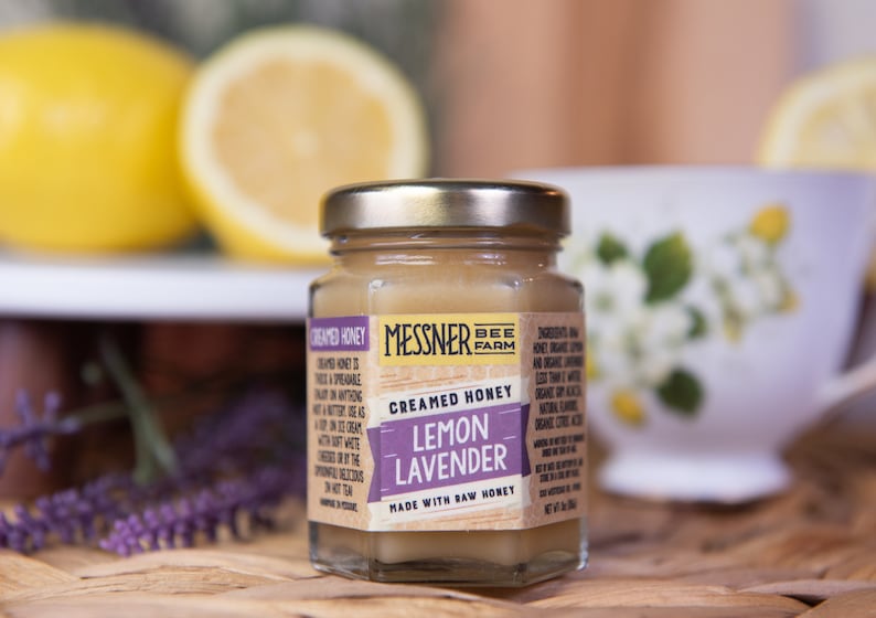 May include: A small glass jar of creamed honey with a brown label that reads 'Messner Bee Farm', 'Creamed Honey', 'Lemon Lavender', and 'Made with Raw Honey'. The jar is sitting on a wooden surface.