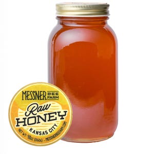 May include: A clear glass jar filled with raw honey, with a gold-colored lid. A round yellow label with the text "Messner Bee Farm Raw Honey Kansas City" is on the left. The jar contains 48 oz of honey.