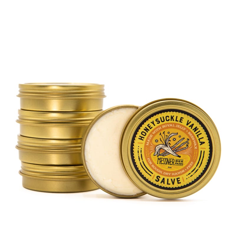 May include: A stack of gold tins of Honeysuckle Vanilla Salve, made with royal jelly and beeswax, by Messner Bee Farm. The salve is for rough, dry hands and feet.