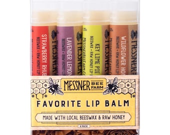 May include: A clear plastic box containing four lip balm tubes labeled Strawberry Rhubarb, Lavender Lemon, Key Lime Pie, and Wildflower Honey. The packaging features a yellow label with the text Messner Bee Farm Favorite Lip Balm.
