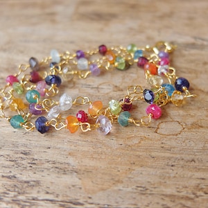 May include: A delicate bracelet featuring a gold-toned chain interspersed with small, faceted, multi-colored gemstones. The stones display a variety of hues including deep blue, bright pink, orange, green, and clear, all linked by thin gold wire.