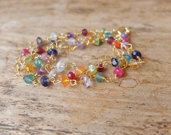 May include: A delicate bracelet featuring a gold-toned chain interspersed with small, faceted, multi-colored gemstones. The stones display a variety of hues including deep blue, bright pink, orange, green, and clear, all linked by thin gold wire.