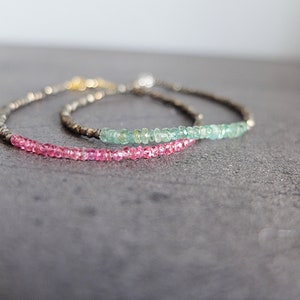 Peut inclure: Deux bracelets délicats avec une chaîne en argent et des perles de pierres précieuses. Le bracelet du haut présente des perles vert clair, tandis que le bracelet du bas présente des perles roses.