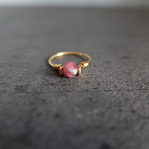 K&ouml;nnte beinhalten: Ein zarter Goldring mit einem rosafarbenen und wei&szlig;en Edelstein, der in Draht gewickelt ist.