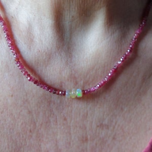 May include: A delicate necklace made of small pink beads with three larger white opal beads in the center.