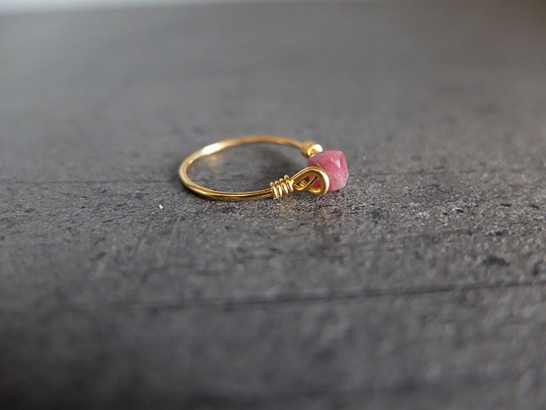 K&ouml;nnte beinhalten: Ein goldener Ring mit einem rosafarbenen Edelstein, der in Draht gewickelt ist.