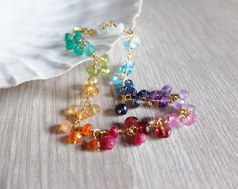 Op de afbeelding: Een kleurrijke edelsteenarmband met een gouden ketting. De armband heeft een kleurengradatie, beginnend met groen en overgaand in geel, oranje, rood, roze, paars en blauw. De edelstenen zijn klein en rond.