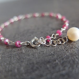 Op de afbeelding: Een delicate zilveren kettingarmband met roze kralen en een enkele witte parelbedel.