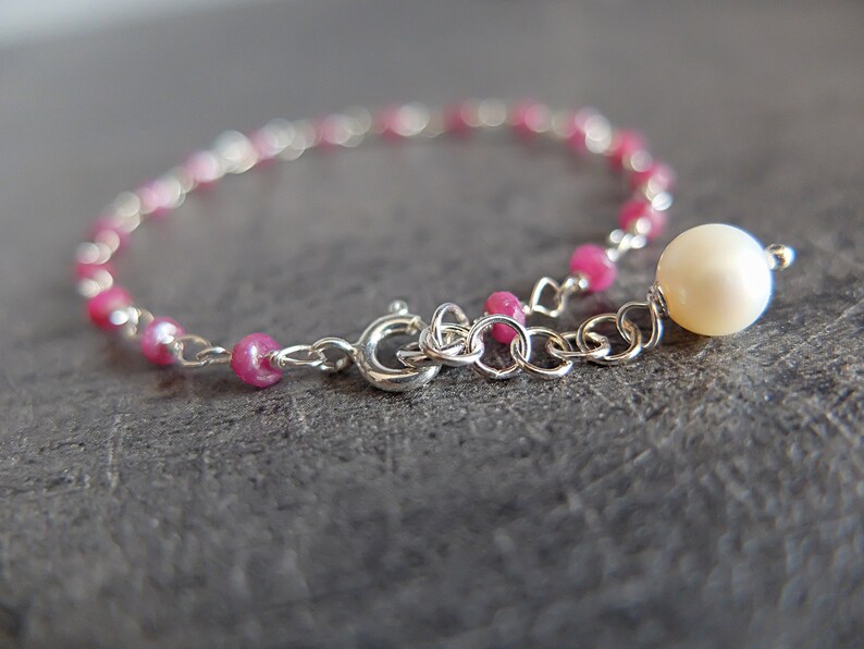 Op de afbeelding: Een delicate zilveren kettingarmband met roze kralen en een enkele witte parelbedel.