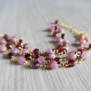 Puede incluir: Un collar de múltiples hilos con cuentas de piedras preciosas rosadas y rojas y eslabones de cadena de oro.
