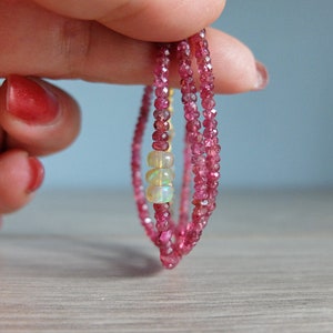 May include: A triple-strand bracelet made of pink tourmaline beads with three opal beads in the center.