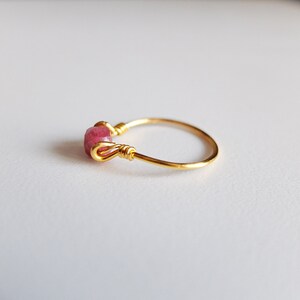 K&ouml;nnte beinhalten: Ein goldener Ring mit einem rosafarbenen Edelstein, der mit Draht umwickelt ist.