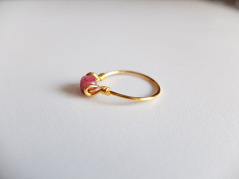 K&ouml;nnte beinhalten: Ein goldener Ring mit einem rosafarbenen Edelstein, der mit Draht umwickelt ist.