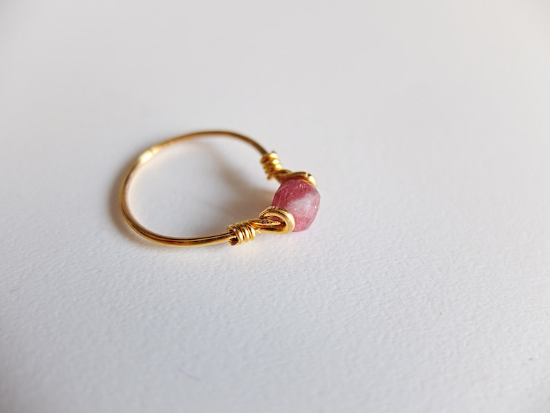 K&ouml;nnte beinhalten: Ein goldener Ring mit einem rosafarbenen Edelstein, der in Draht gewickelt ist.