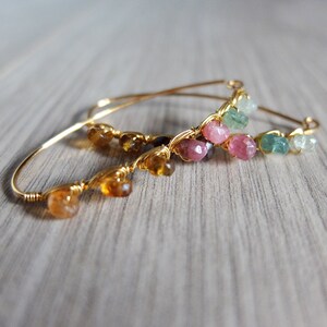 May include: Three gold wire wrapped bracelets with different colored gemstones. The bracelets feature a variety of colors including green, pink, and brown.