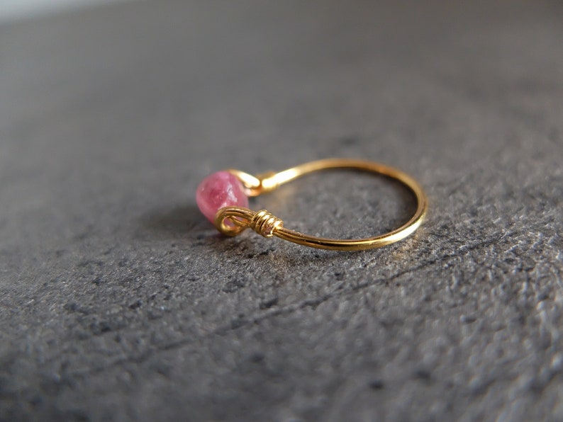 K&ouml;nnte beinhalten: Ein zarter Goldring mit einem rosafarbenen Edelstein, der in die Band eingefasst ist. Der Ring ist schlicht und elegant und perfekt f&uuml;r den Alltag.