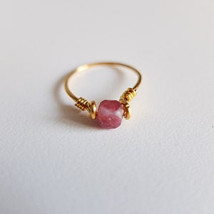 K&ouml;nnte beinhalten: Ein goldener Ring mit einem rosafarbenen Edelstein, der mit Draht umwickelt ist.