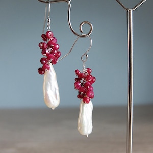 May include: A pair of silver earrings featuring a cluster of red ruby stones and a white pearl drop on each earring.
